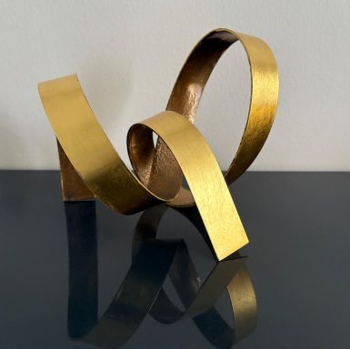 Goldene, geschwungene Skulptur auf einem glatten, reflektierenden Tisch.
